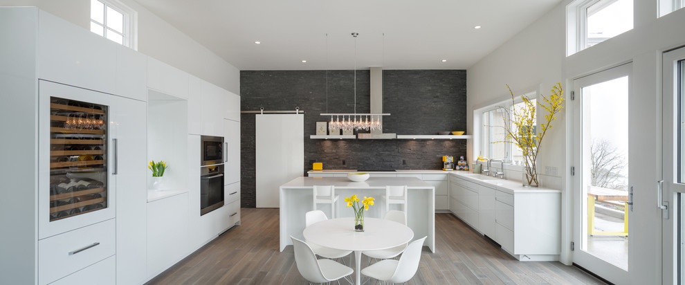 Moderne Wohnküche in L-Form mit flächenbündigen Schrankfronten, weißen Schränken, Elektrogeräten mit Frontblende, Küchenrückwand in Grau und Rückwand aus Schiefer in Portland