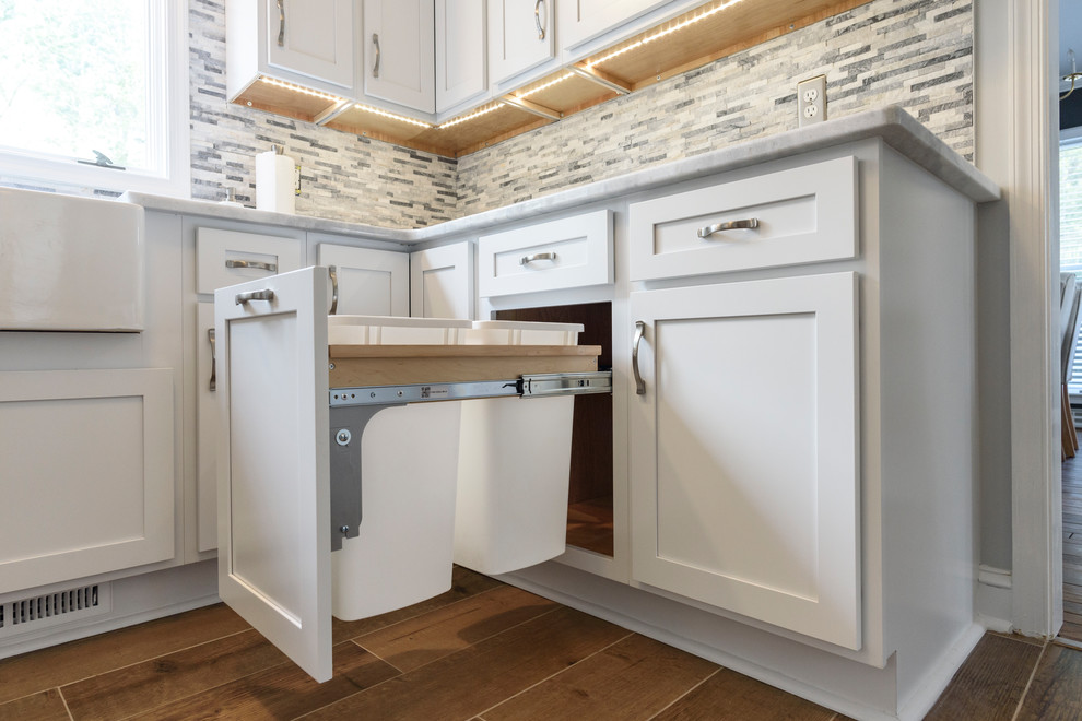 Example of a large transitional l-shaped ceramic tile and brown floor eat-in kitchen design in Baltimore with a farmhouse sink, shaker cabinets, white cabinets, granite countertops, gray backsplash, stone tile backsplash, stainless steel appliances, no island and white countertops