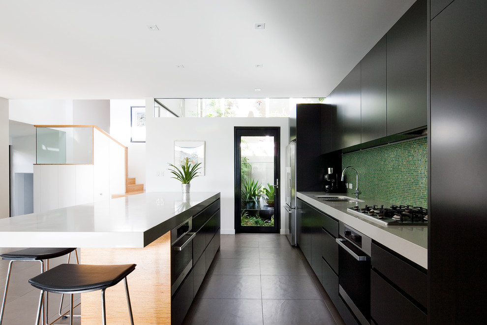 Modelo de cocina contemporánea con armarios con paneles lisos, puertas de armario negras, salpicadero gris, electrodomésticos de acero inoxidable y suelo gris