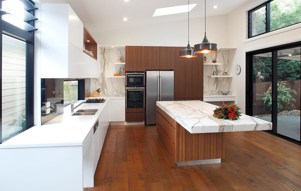 Foto på ett mellanstort funkis kök, med en dubbel diskho, släta luckor, skåp i mellenmörkt trä, marmorbänkskiva, vitt stänkskydd, stänkskydd i sten, rostfria vitvaror, mellanmörkt trägolv och en köksö