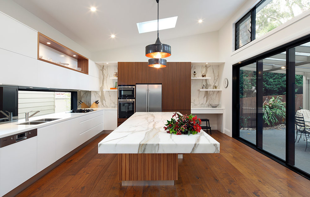 Modern inredning av ett mellanstort kök, med en dubbel diskho, släta luckor, skåp i mellenmörkt trä, marmorbänkskiva, vitt stänkskydd, stänkskydd i sten, rostfria vitvaror, mellanmörkt trägolv och en köksö