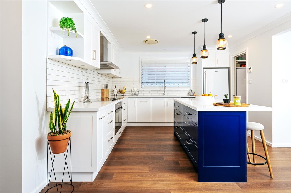 Photo of a medium sized contemporary l-shaped kitchen in Other with white cabinets, composite countertops, white splashback, ceramic splashback, white appliances, dark hardwood flooring, an island, brown floors, white worktops and recessed-panel cabinets.