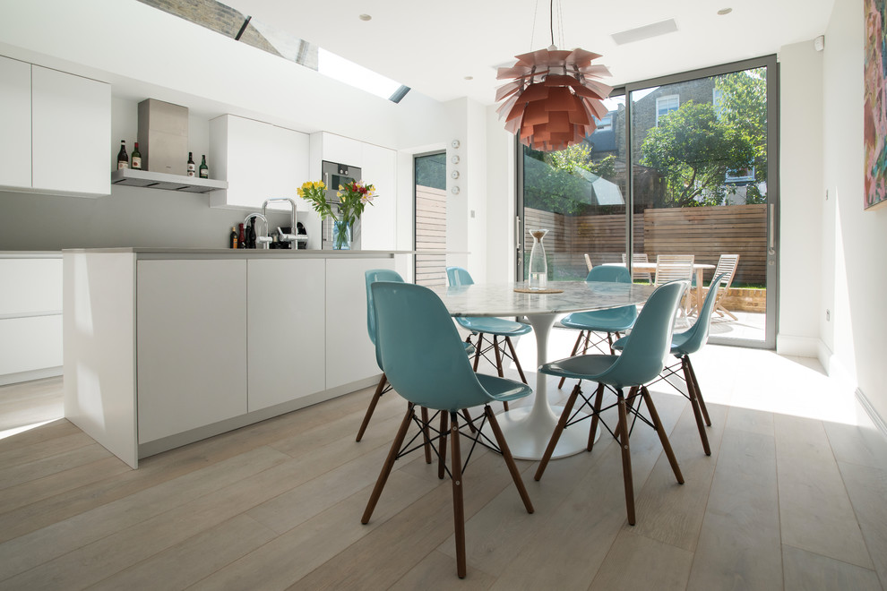 Design ideas for a medium sized contemporary kitchen/diner in London with white cabinets, composite countertops, grey splashback, an island, flat-panel cabinets and light hardwood flooring.