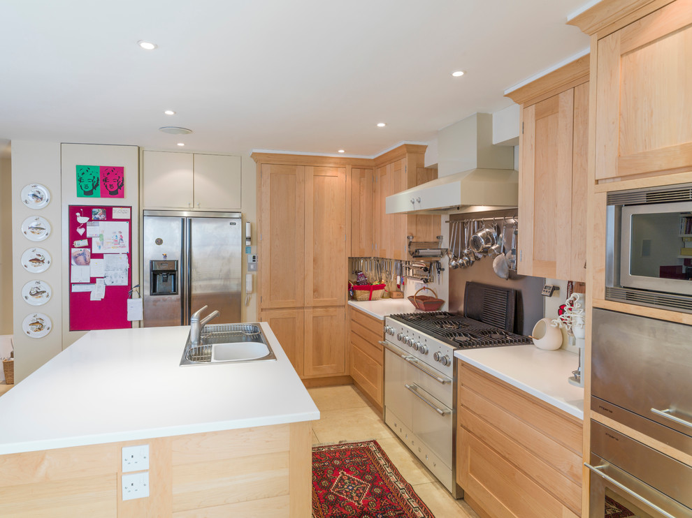 This is an example of a medium sized modern galley open plan kitchen in Other with a triple-bowl sink, recessed-panel cabinets, light wood cabinets, composite countertops, metallic splashback, stainless steel appliances, limestone flooring and an island.
