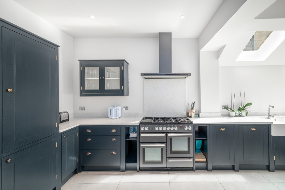 Skandinavische Küche in L-Form mit Landhausspüle, flächenbündigen Schrankfronten, blauen Schränken, Küchenrückwand in Grau, Elektrogeräten mit Frontblende, weißem Boden und weißer Arbeitsplatte in London