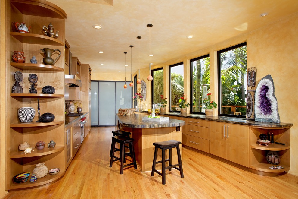 Cette image montre une cuisine américaine parallèle ethnique en bois clair avec un placard à porte plane, un plan de travail en granite, parquet clair et îlot.