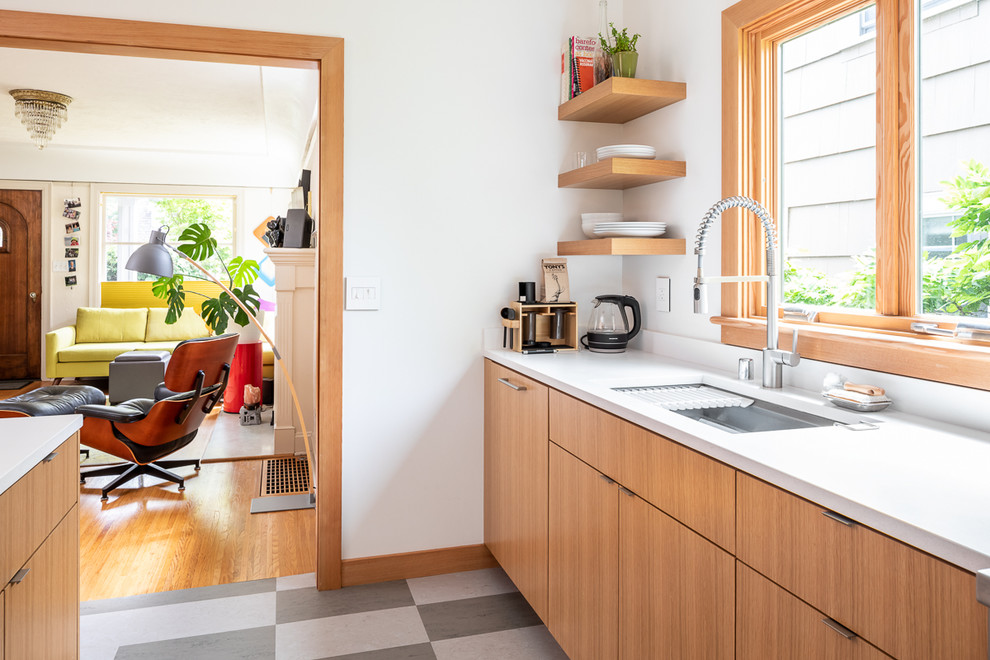 Inspiration for a small modern kitchen in Seattle with a submerged sink, flat-panel cabinets, light wood cabinets, engineered stone countertops, white splashback, ceramic splashback, stainless steel appliances, lino flooring, an island, multi-coloured floors and white worktops.