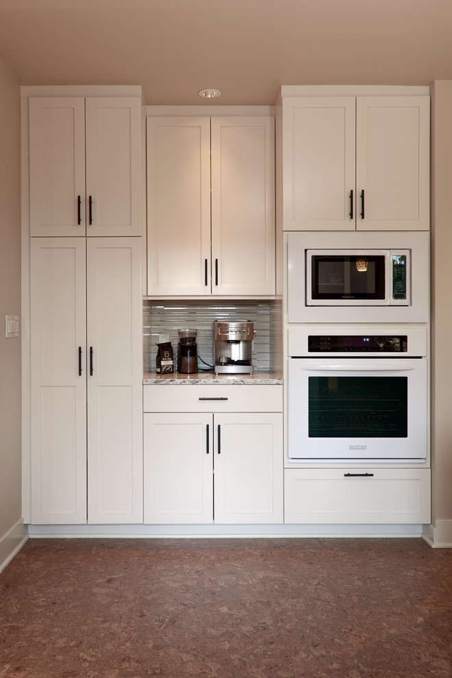 Medium sized traditional single-wall kitchen/diner in Seattle with shaker cabinets, white cabinets, white appliances, cork flooring, an island, beige splashback, a submerged sink, quartz worktops, glass tiled splashback and brown floors.