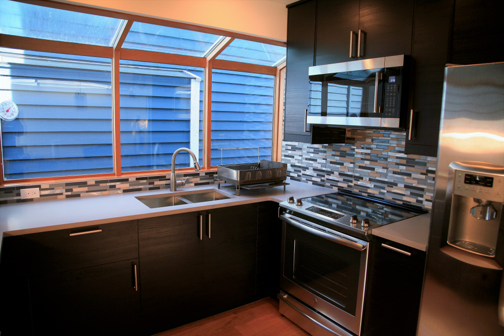 シアトルにある低価格の小さなコンテンポラリースタイルのおしゃれなキッチン (ダブルシンク、フラットパネル扉のキャビネット、黒いキャビネット、人工大理石カウンター、青いキッチンパネル、ボーダータイルのキッチンパネル、シルバーの調理設備、淡色無垢フローリング、ベージュの床、グレーのキッチンカウンター) の写真