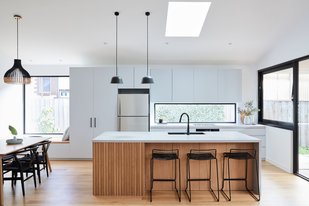 Modern inredning av ett mellanstort grå grått kök, med en undermonterad diskho, grå skåp, bänkskiva i betong, fönster som stänkskydd, ljust trägolv, en köksö, släta luckor, rostfria vitvaror och beiget golv