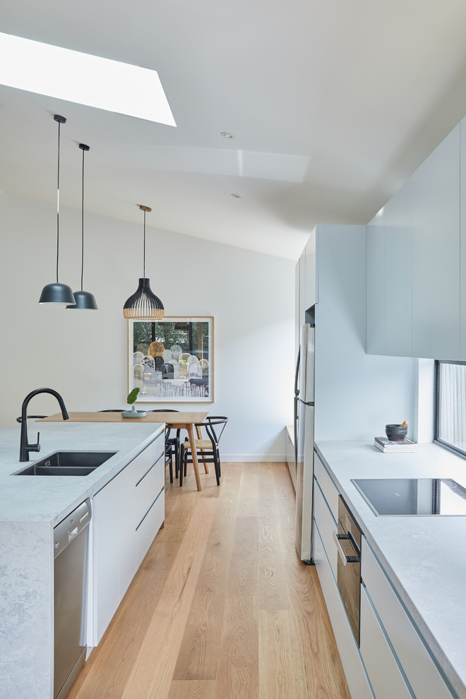 Foto på ett mellanstort funkis grå kök, med en undermonterad diskho, släta luckor, grå skåp, bänkskiva i betong, fönster som stänkskydd, rostfria vitvaror, ljust trägolv, en köksö och beiget golv