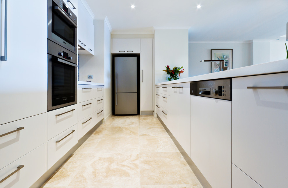Photo of a small modern galley kitchen in Sydney with flat-panel cabinets, white cabinets, engineered stone countertops, multi-coloured splashback, glass tiled splashback, stainless steel appliances, a double-bowl sink and travertine flooring.
