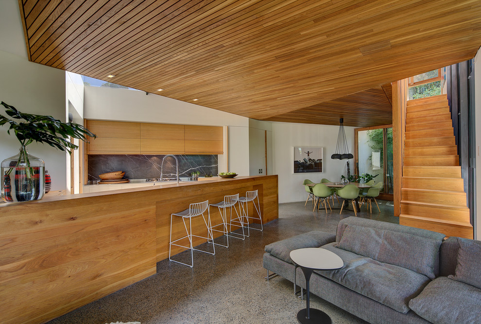На фото: кухня-гостиная в современном стиле с плоскими фасадами, фасадами цвета дерева среднего тона, серым фартуком и островом