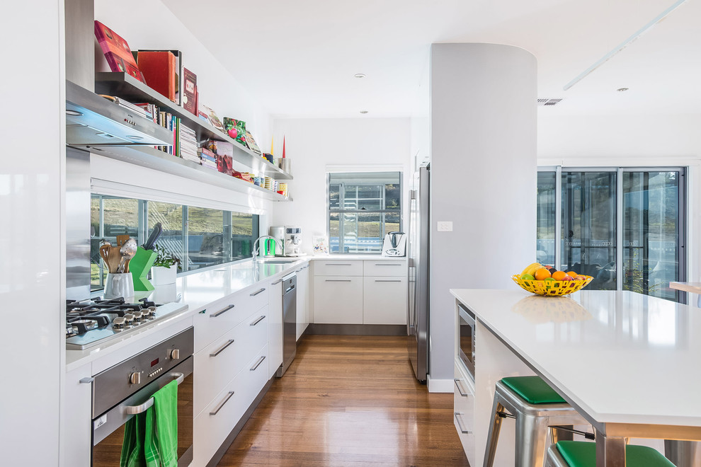 Moderne Küche mit flächenbündigen Schrankfronten, weißen Schränken, Küchengeräten aus Edelstahl, braunem Holzboden und Kücheninsel in Hobart