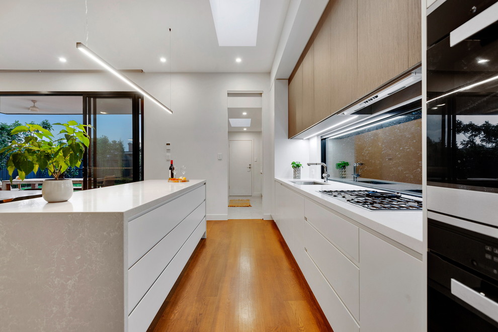 This is an example of a medium sized modern single-wall open plan kitchen in Melbourne with a submerged sink, flat-panel cabinets, white cabinets, engineered stone countertops, window splashback, stainless steel appliances, an island and white worktops.