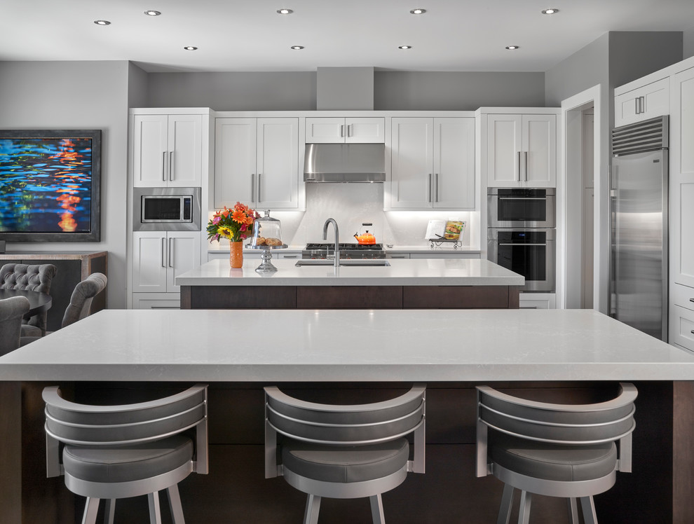 Design ideas for an expansive contemporary l-shaped open plan kitchen in Edmonton with a submerged sink, white cabinets, engineered stone countertops, white splashback, stone tiled splashback, stainless steel appliances, multiple islands, white worktops and shaker cabinets.