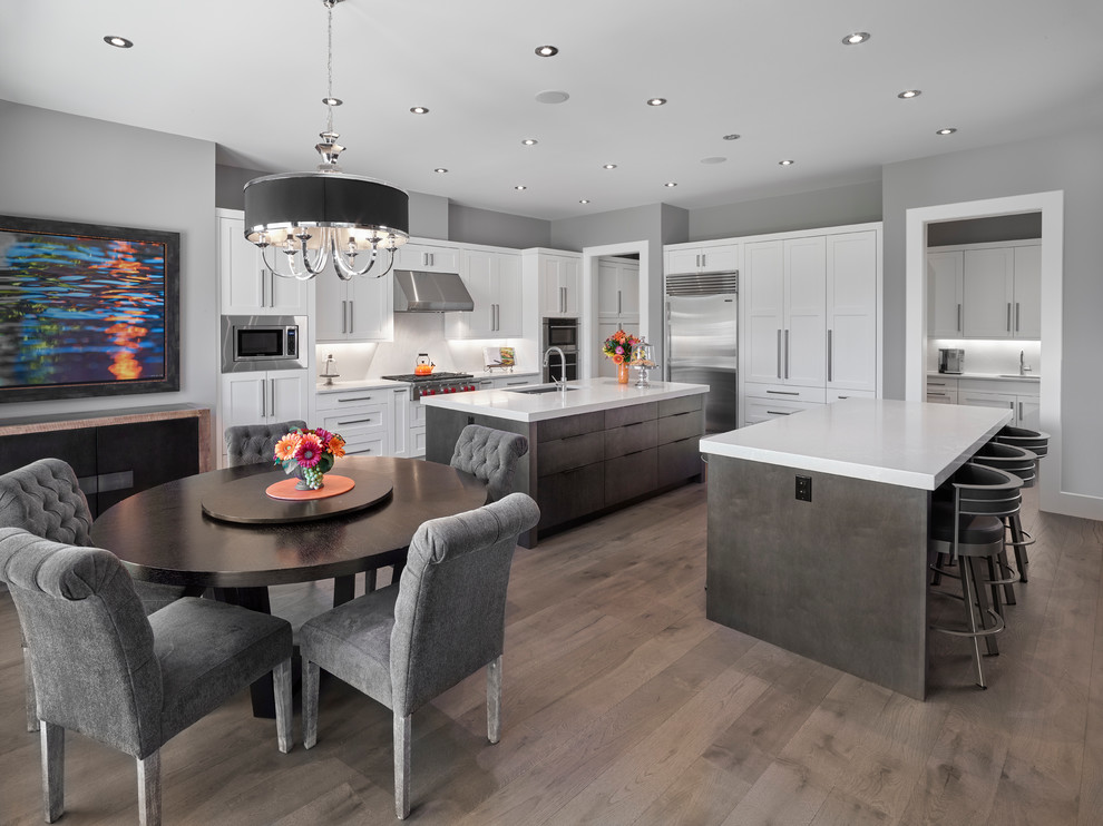 Inspiration for an expansive classic l-shaped open plan kitchen in Edmonton with flat-panel cabinets, white cabinets, engineered stone countertops, white splashback, multiple islands, white worktops, a submerged sink, stone tiled splashback, stainless steel appliances, light hardwood flooring and brown floors.
