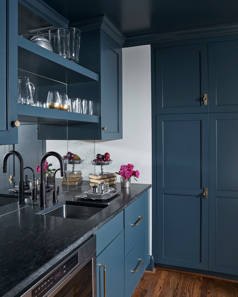 Inredning av ett klassiskt grå grått kök, med en undermonterad diskho, blå skåp, spegel som stänkskydd och mellanmörkt trägolv