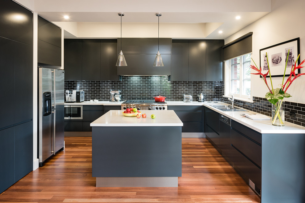 Inspiration for an expansive contemporary u-shaped open plan kitchen in Melbourne with a double-bowl sink, flat-panel cabinets, black cabinets, engineered stone countertops, black splashback, glass tiled splashback, stainless steel appliances, medium hardwood flooring and an island.