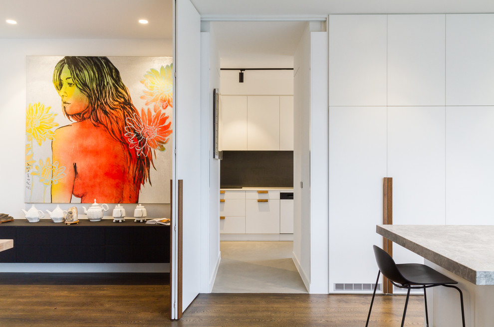 This is an example of a large modern l-shaped open plan kitchen in Melbourne with a submerged sink, flat-panel cabinets, white cabinets, grey splashback, marble splashback, black appliances, medium hardwood flooring, an island, brown floors, grey worktops and limestone worktops.