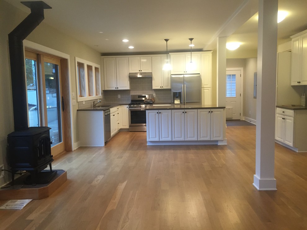 Bild på ett mellanstort amerikanskt kök, med en nedsänkt diskho, luckor med upphöjd panel, vita skåp, bänkskiva i kvarts, grått stänkskydd, stänkskydd i glaskakel, rostfria vitvaror, ljust trägolv, en köksö och brunt golv
