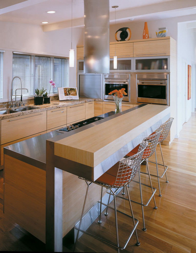 Idée de décoration pour une cuisine design en bois clair avec un plan de travail en granite, un placard à porte plane et un électroménager en acier inoxydable.