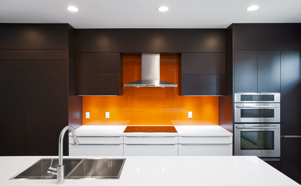 Inredning av ett modernt linjärt kök och matrum, med en nedsänkt diskho, släta luckor, bruna skåp, bänkskiva i kvarts, orange stänkskydd, glaspanel som stänkskydd och integrerade vitvaror