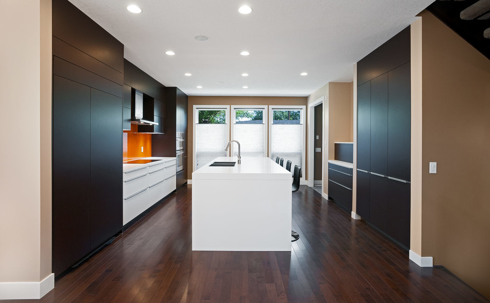 Modern inredning av ett linjärt kök och matrum, med en nedsänkt diskho, släta luckor, bruna skåp, bänkskiva i kvarts, orange stänkskydd, glaspanel som stänkskydd och integrerade vitvaror
