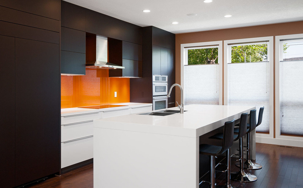 Exempel på ett modernt linjärt kök och matrum, med en nedsänkt diskho, släta luckor, bruna skåp, bänkskiva i kvarts, orange stänkskydd, glaspanel som stänkskydd och integrerade vitvaror