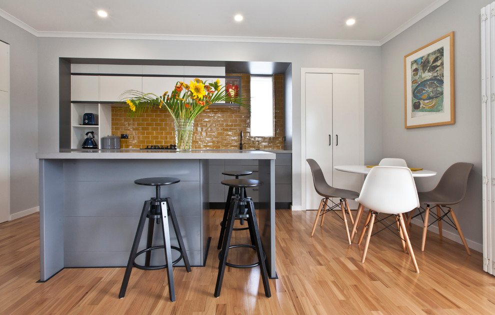 Modern inredning av ett kök, med släta luckor, grå skåp, gult stänkskydd, ljust trägolv och en köksö