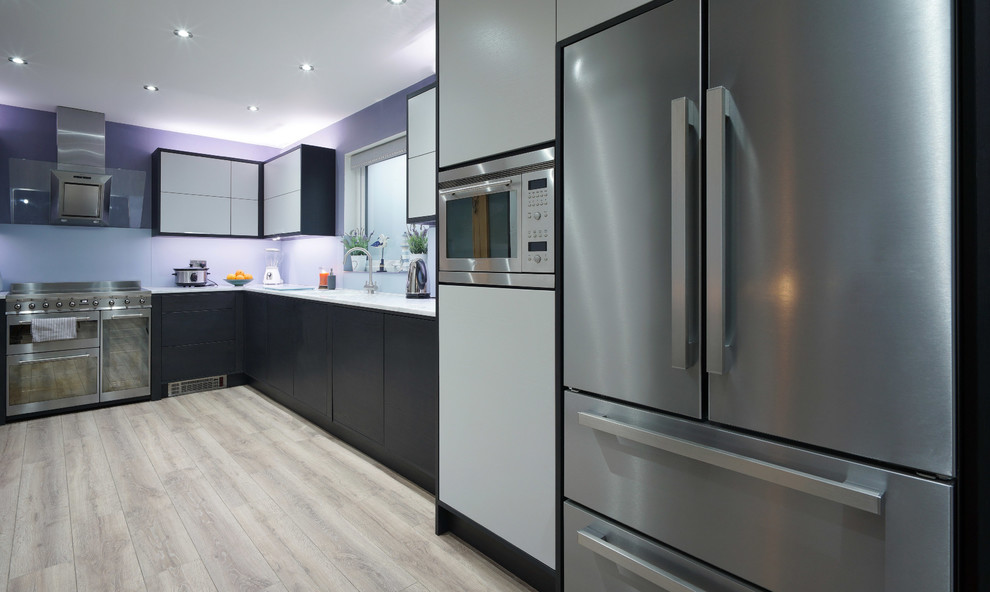 Photo of a medium sized modern l-shaped open plan kitchen in Other with an integrated sink, flat-panel cabinets, grey cabinets, composite countertops, grey splashback, glass sheet splashback, stainless steel appliances, laminate floors and no island.