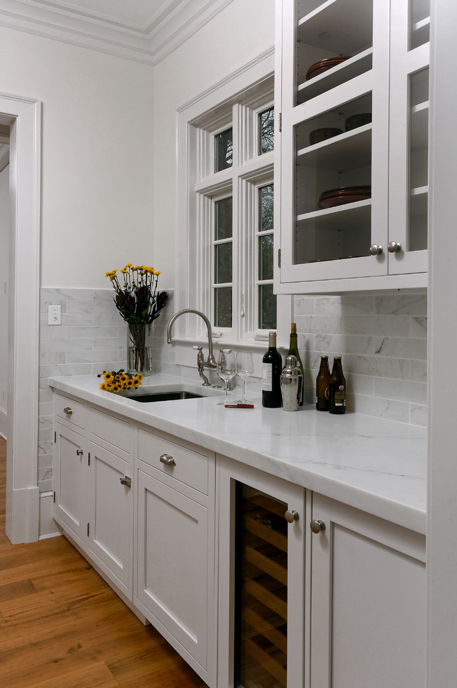 Bild på ett mellanstort vintage kök, med en undermonterad diskho, vita skåp, marmorbänkskiva, vitt stänkskydd, stänkskydd i stenkakel, rostfria vitvaror, ljust trägolv och en köksö