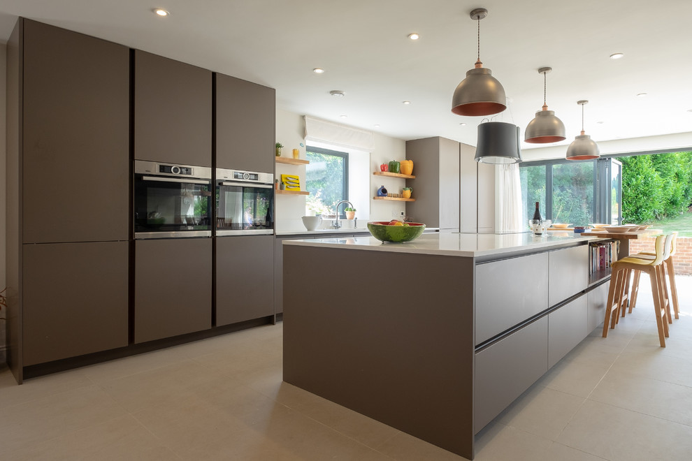 This is an example of an expansive contemporary single-wall kitchen in Hampshire with an integrated sink, flat-panel cabinets, composite countertops, stainless steel appliances, porcelain flooring and an island.