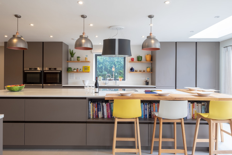 Inspiration for an expansive contemporary galley kitchen in Hampshire with flat-panel cabinets, composite countertops, stainless steel appliances, porcelain flooring, an island, grey cabinets, grey floors and white worktops.