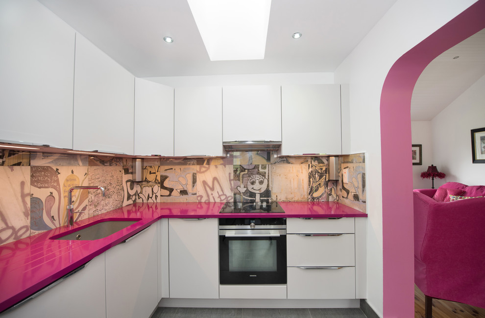 На фото: угловая кухня среднего размера в стиле фьюжн с плоскими фасадами, техникой из нержавеющей стали, серым полом, белыми фасадами, разноцветным фартуком и розовой столешницей с