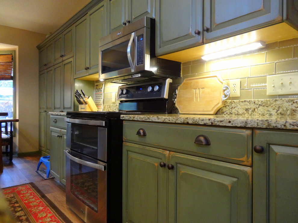 Inredning av ett rustikt mellanstort kök, med en dubbel diskho, luckor med upphöjd panel, gröna skåp, granitbänkskiva, beige stänkskydd, stänkskydd i tunnelbanekakel, rostfria vitvaror, mellanmörkt trägolv och en halv köksö