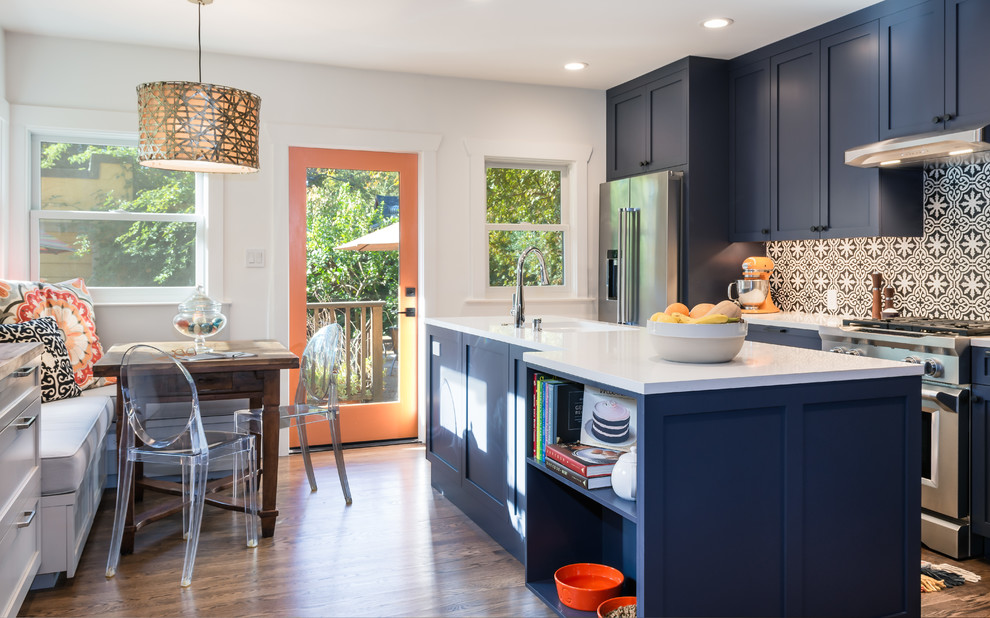 Idée de décoration pour une cuisine parallèle tradition avec un évier encastré, un placard à porte shaker, des portes de placard bleues, un plan de travail en quartz modifié, une crédence multicolore, une crédence en carreau de ciment, un électroménager en acier inoxydable, un sol en bois brun, îlot, un sol marron et un plan de travail blanc.