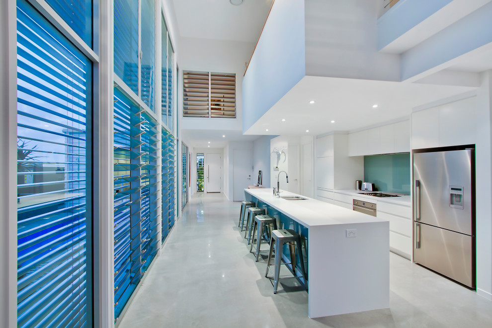 Design ideas for a contemporary galley kitchen in Gold Coast - Tweed with a submerged sink, flat-panel cabinets, white cabinets, blue splashback, glass sheet splashback, stainless steel appliances, an island, grey floors and white worktops.