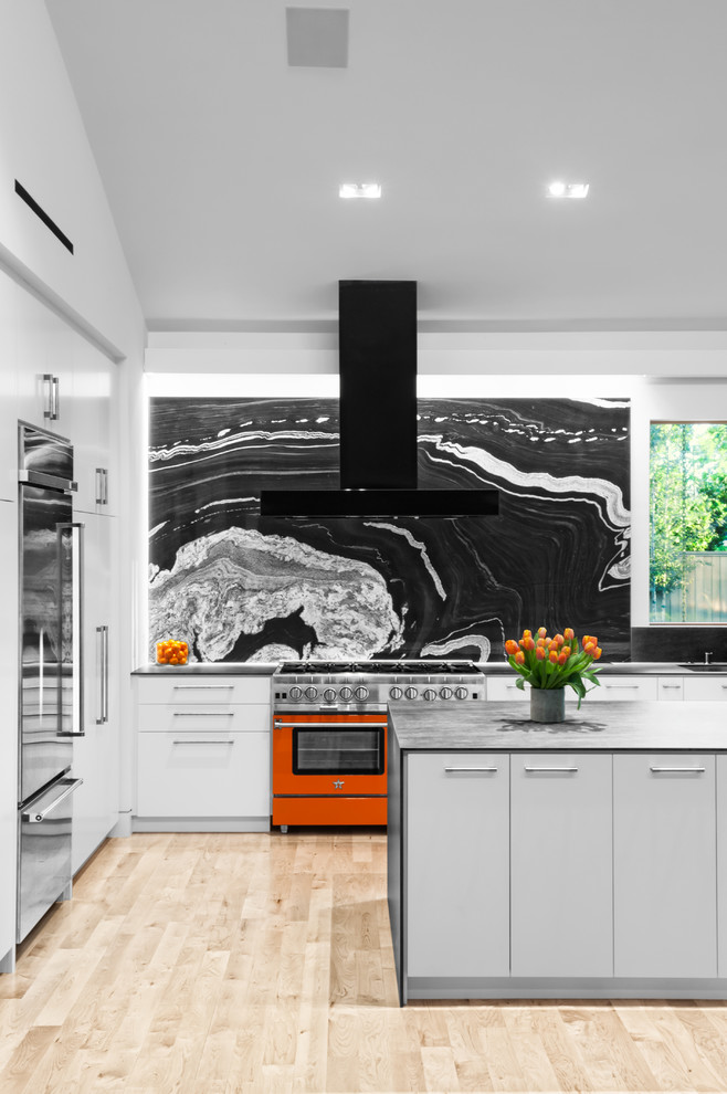 Diseño de cocinas en L contemporánea con armarios con paneles lisos, puertas de armario blancas, salpicadero negro, electrodomésticos de colores, suelo de madera clara, una isla y suelo beige