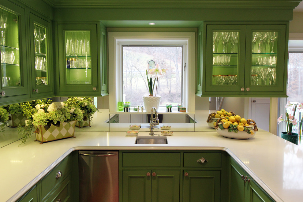 Inredning av ett klassiskt mellanstort kök, med en undermonterad diskho, luckor med glaspanel, gröna skåp, bänkskiva i glas, vitt stänkskydd, spegel som stänkskydd, rostfria vitvaror och mellanmörkt trägolv