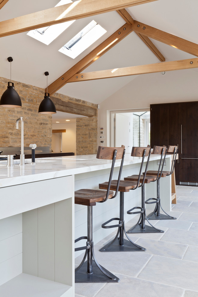 Photo of a large contemporary galley open plan kitchen in Gloucestershire with marble worktops, limestone flooring, an island, an integrated sink and black appliances.