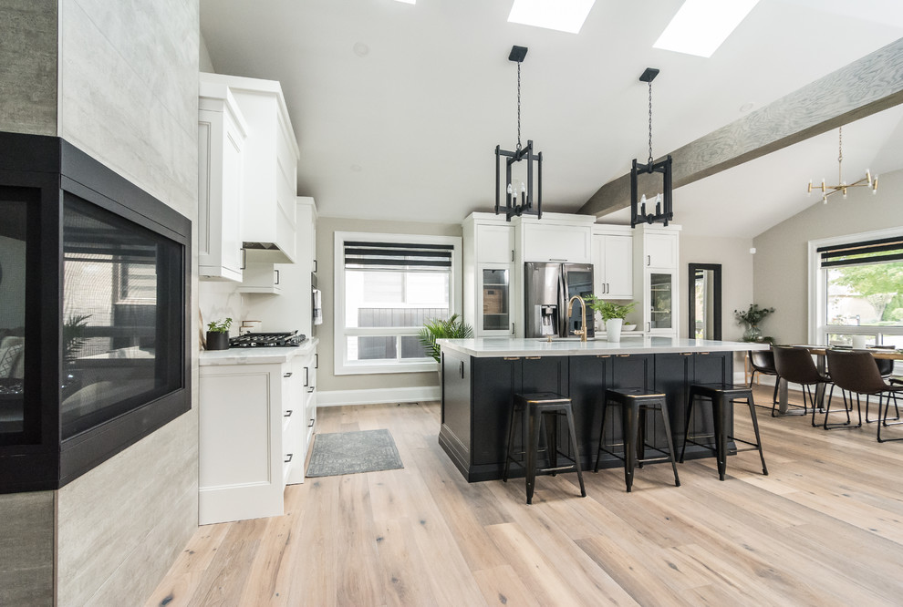 This is an example of a large traditional l-shaped kitchen/diner in Toronto with a submerged sink, shaker cabinets, white cabinets, engineered stone countertops, white splashback, stone slab splashback, black appliances, medium hardwood flooring, an island, brown floors and white worktops.