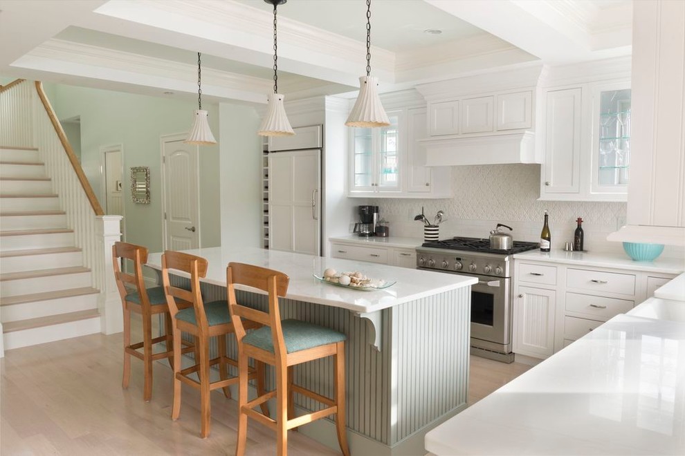 Klassische Küche in L-Form mit weißen Schränken, Küchenrückwand in Weiß, hellem Holzboden, Kücheninsel, Rückwand aus Keramikfliesen und Elektrogeräten mit Frontblende in Boston