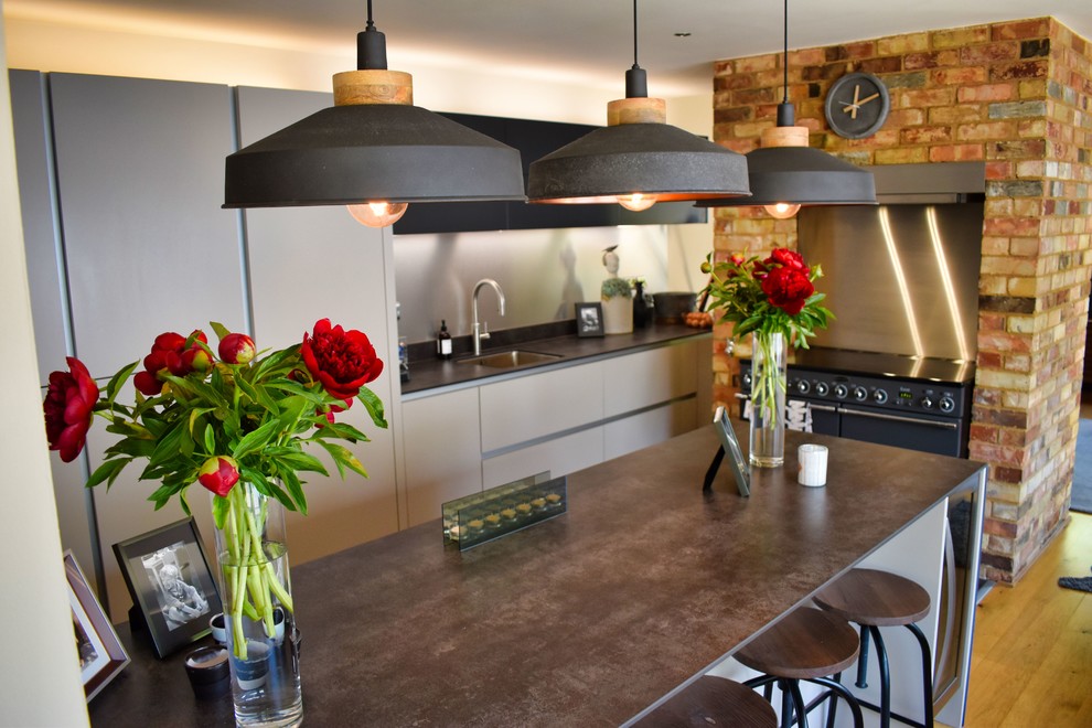 Example of a large trendy galley dark wood floor eat-in kitchen design in Cambridgeshire with a triple-bowl sink, flat-panel cabinets, black appliances, a peninsula and black countertops