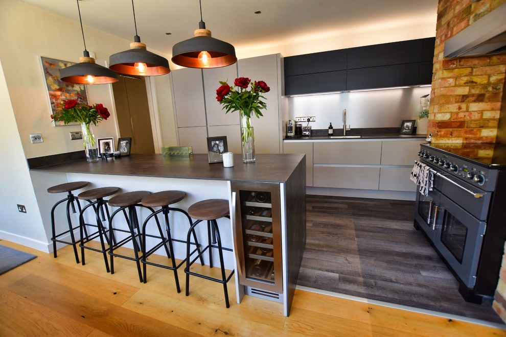 Photo of a large contemporary kitchen/diner in Cambridgeshire with a submerged sink, flat-panel cabinets, beige cabinets, black appliances, light hardwood flooring, an island and grey worktops.