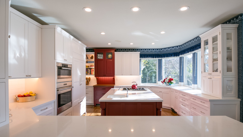 Inspiration for a large traditional u-shaped enclosed kitchen in San Francisco with a submerged sink, shaker cabinets, white cabinets, composite countertops, white splashback, ceramic splashback, integrated appliances, medium hardwood flooring and an island.