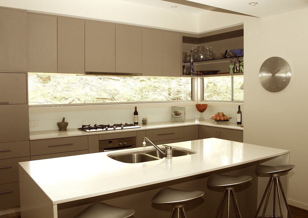 Immagine di una cucina minimal con lavello sottopiano, ante lisce, ante grigie, top in superficie solida, paraspruzzi bianco, paraspruzzi con lastra di vetro e elettrodomestici in acciaio inossidabile