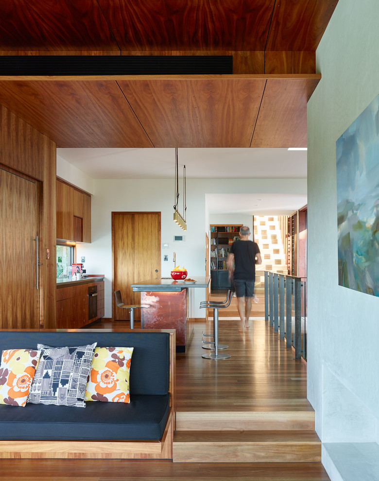На фото: параллельная кухня среднего размера в современном стиле с фасадами цвета дерева среднего тона, столешницей из бетона, черной техникой, паркетным полом среднего тона и островом
