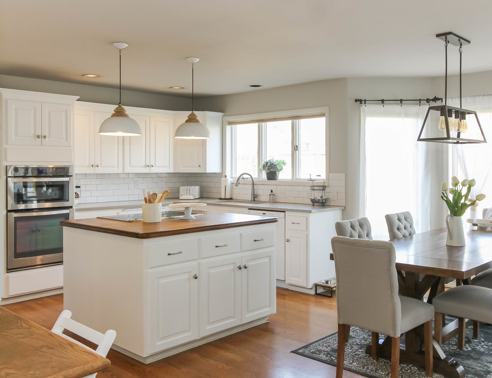This is an example of a medium sized rural u-shaped kitchen/diner in Seattle with a submerged sink, raised-panel cabinets, white cabinets, engineered stone countertops, white splashback, metro tiled splashback, stainless steel appliances, medium hardwood flooring, an island and brown floors.