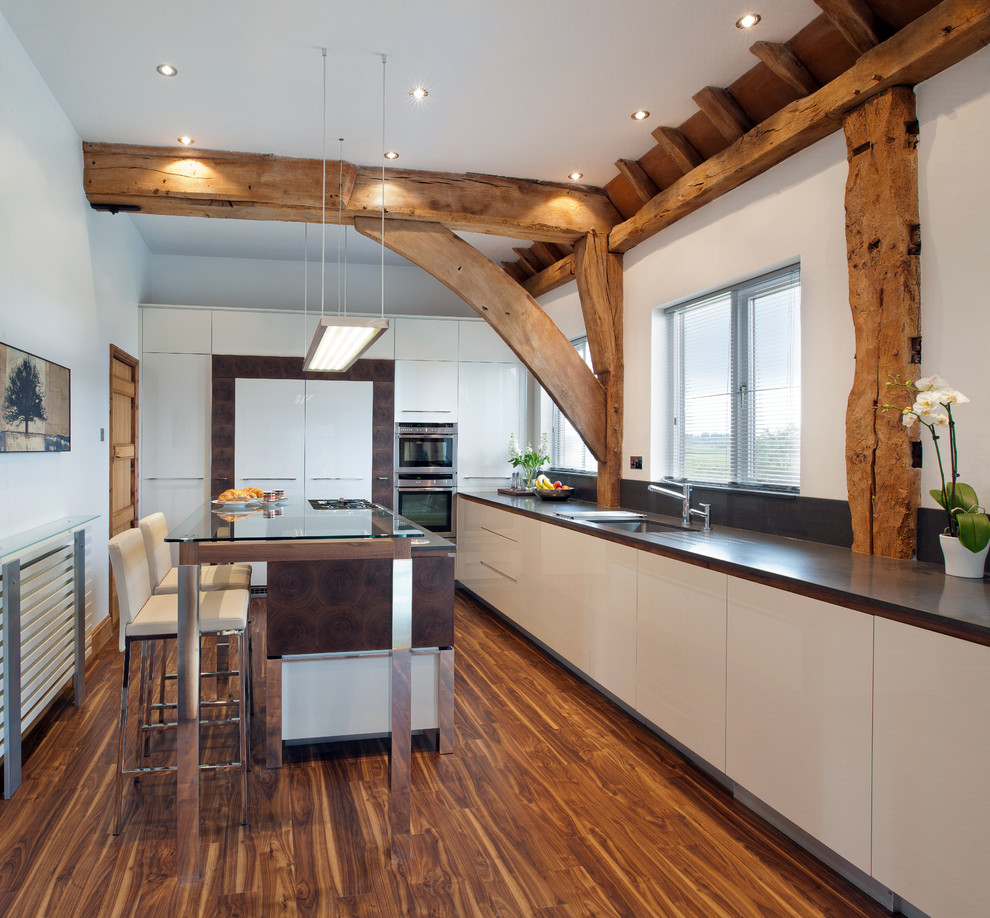 Cette image montre une cuisine design en L et bois foncé fermée avec un placard à porte plane, un plan de travail en quartz, un électroménager en acier inoxydable, îlot et un sol en bois brun.